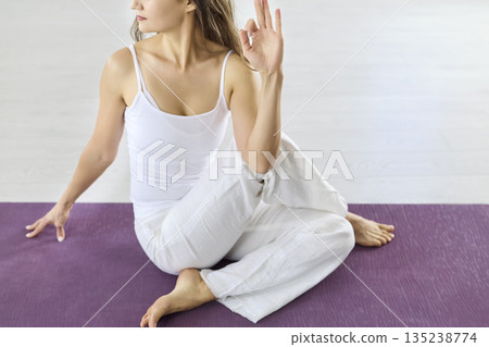 Closeup of woman performing seated spinal twist yoga with hand mudra on mat 135238774