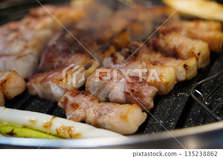 Sizzling Korean pork belly (samgyeopsal) grilling on a hot barbecue, close-up shot. 135238862