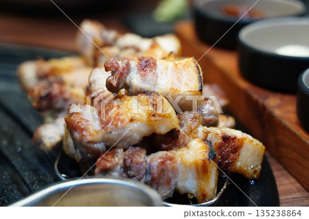 Sizzling Korean pork belly (samgyeopsal) grilling on a hot barbecue, close-up shot. 135238864