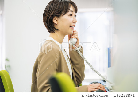 Young woman answering the phone in the office 135238871