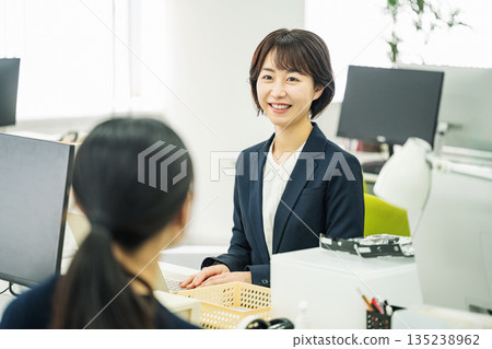 年輕女子在辦公室的辦公桌旁與同事交談 135238962