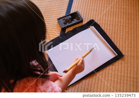 一位女孩在榻榻米上寫書法。 135239473