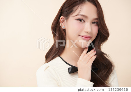 A beautiful young Asian woman with clean, fresh skin against a beige background. Skincare, facial treatment, cosmetology, beauty, and spa. An elegant portrait of an Asian woman. 135239616