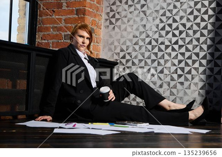 Businessperson leaning on brick ledge with documents and coffee Businessperson leaning on brick ledge with documents and coffee 135239656