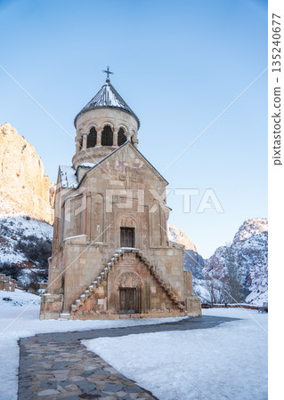 Noravank Monastery stands in snow-covered mountain gorge in Armenia, dramatic red cliffs, winter light, architectural presence, serene atmosphere Noravank Monastery stands in snow-covered mountain gorge in Armenia, dramatic red cliffs, winter light, architectural presence, serene atmosphere 135240677