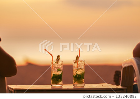Two mojito cocktails served in glasses at sunset. A couple's vacation at resorts and entertainment, a honeymoon trip. Two people are watching the sunset sitting in sun beds and drinking cocktails Two mojito cocktails served in glasses at sunset. A couple's vacation at resorts and entertainment, a honeymoon trip. Two people are watching the sunset sitting in sun beds and drinking cocktails 135240882