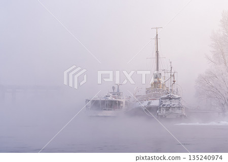 The outlines and silhouettes of old river ships moored to the shore in the winter fog. nostalgic art plot, historical heritage. High quality photo 135240974
