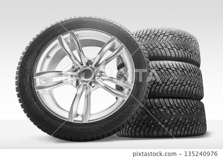 A set of four winter tires with studded features is presented alongside an alloy wheel. This setup is ideal for tire replacement, enhancing traction and safety 135240976