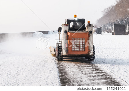 Clearing snow from sidewalks in winter with the help of a mini loader and municipal snow removal equipment. Snowfall and ice, danger of slipping and falling, injury and fractures. High quality photo 135241021