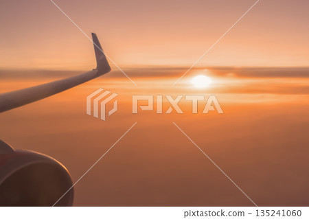 An orange sunset above the clouds and a red sun are the wings of an airplane in flight . Air travel and ticket sales are a beautiful background concept. High quality photo 135241060