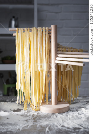 Homemade noodles hanging on wooden noodle dryer rack. Home cooking concept Homemade noodles hanging on wooden noodle dryer rack. Home cooking concept 135241286