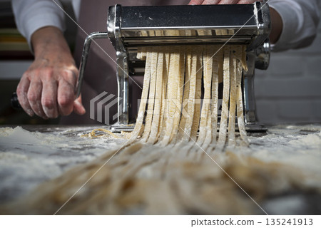 Caucasian female hands making fettuccine noodles using mechanical pasta machine Caucasian female hands making fettuccine noodles using mechanical pasta machine 135241913