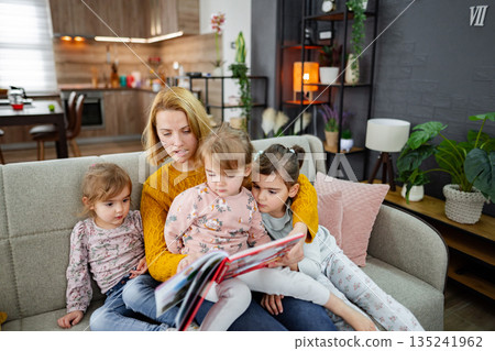 Mother looks at a book and reads a story to her daughters 135241962