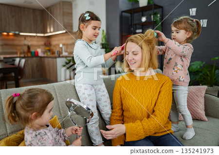 Three little girls are doing their mom's hair 135241973
