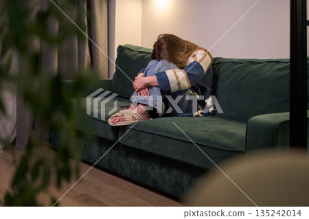 Female curled up on green sofa indoors Female curled up on green sofa indoors 135242014