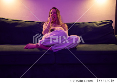 Female watching screen while eating popcorn in cozy living room Female watching screen while eating popcorn in cozy living room 135242016