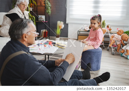 Grandfather draws a girl in a cozy living room 135242017