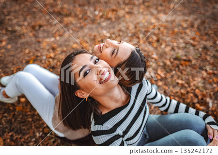 Girls enjoying a cozy autumn day together in the colorful leaves of the park Girls enjoying a cozy autumn day together in the colorful leaves of the park 135242172