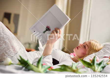 Woman reading magazine, Caucasian female relaxing in bed with tulips during tranquil afternoon rest Woman reading magazine, Caucasian female relaxing in bed with tulips during tranquil afternoon rest 135242554