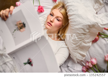 Relaxed woman examining magazine pages, Caucasian woman carefully editing magazine pages in warm sunlight Relaxed woman examining magazine pages, Caucasian woman carefully editing magazine pages in warm sunlight 135242557