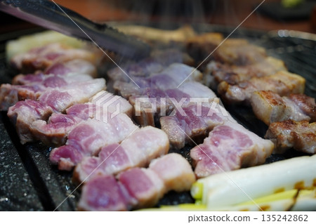 Sizzling Korean pork belly (samgyeopsal) grilling on a hot barbecue grill plate 135242862