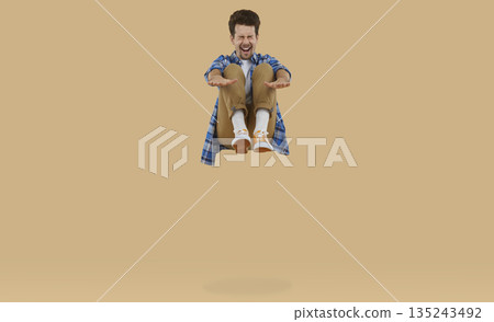 Happy, cheerful, funny, excited young man screaming while jumping up high on a trampoline 135243492