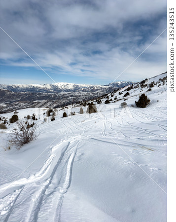 Ski track in white snow going down a mountain slope. Winter mountain landscape Ski track in white snow going down a mountain slope. Winter mountain landscape 135243515