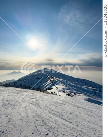 Sun over snowy mountain slope at Amirsoy ski resort. Winter landscape Sun over snowy mountain slope at Amirsoy ski resort. Winter landscape 135243520
