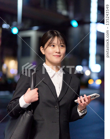 A young businesswoman walking through the city at night with a bright expression A young businesswoman walking through the city at night with a bright expression 135243549