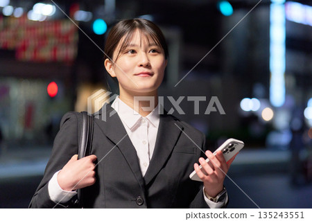 A woman in a suit walking home from work with a smartphone in her hand A woman in a suit walking home from work with a smartphone in her hand 135243551