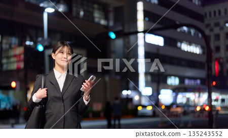 A young businesswoman walking through the city at night with a bright expression A young businesswoman walking through the city at night with a bright expression 135243552