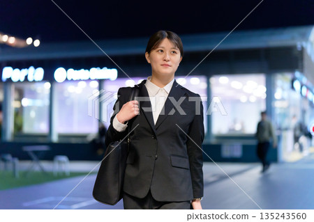 一位身著職業套裝的年輕女商人在夜間走在城市裡。 135243560