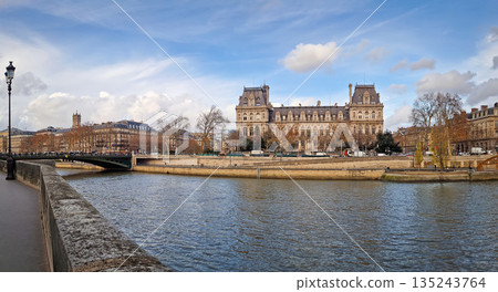 Beautiful panoramic view of the Hotel de Ville from the Seine riverside, showing the grand Neo-Renaissance facade and the riverbanks lined with trees and stone embankments Beautiful panoramic view of the Hotel de Ville from the Seine riverside, showing the grand Neo-Renaissance facade and the riverbanks lined with trees and stone embankments 135243764