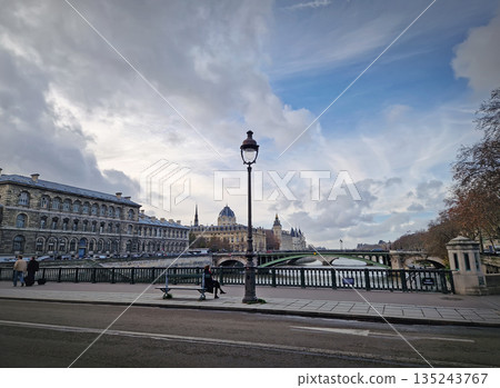 Paris, France - December 10, 2025: Scenic parisian view with the Seine River and the Arcole Bridge. The historic stone facade of the Hotel-Dieu and the Conciergerie towers Paris, France - December 10, 2025: Scenic parisian view with the Seine River and the Arcole Bridge. The historic stone facade of the Hotel-Dieu and the Conciergerie towers 135243767