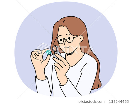 Woman jeweler examines gemstone through magnifying glass, checking diamond for authenticity 135244463