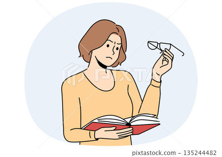 Woman experiences vision problems reading book and looks at glasses with upset grimace 135244482