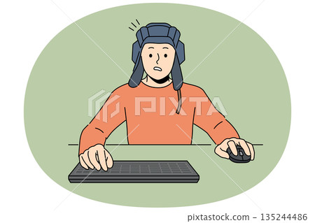 Man gamer plays tanks on computer, sitting at table with keyboard and wears tanker helmet 135244486