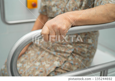 Asian elderly woman patient use toilet support rail in bathroom. Asian elderly woman patient use toilet support rail in bathroom. 135244692