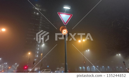 Foggy night city street with amber traffic light and yield sign Foggy night city street with amber traffic light and yield sign 135244852