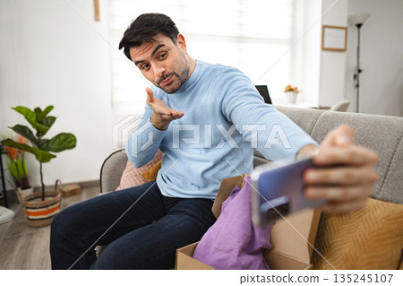 Grateful men talking on a video call while unboxing a gift Grateful men talking on a video call while unboxing a gift 135245107