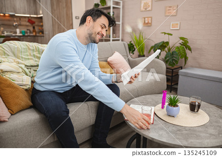 Smiling man sitting on house looking at bills and drinking drink Smiling man sitting on house looking at bills and drinking drink 135245109
