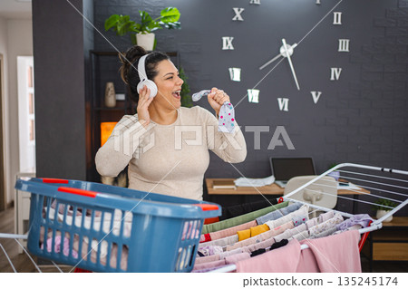 Woman singing while hanging the laundry on drying rack at home Woman singing while hanging the laundry on drying rack at home 135245174