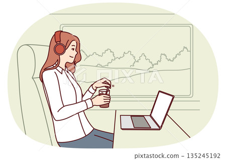 Woman train passenger uses laptop working on trip and drinks coffee sitting near large window 135245192