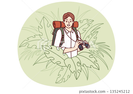 Man traveler stands in thickets of jungle and holds binoculars exploring area in search further path Man traveler stands in thickets of jungle and holds binoculars exploring area in search further path 135245212