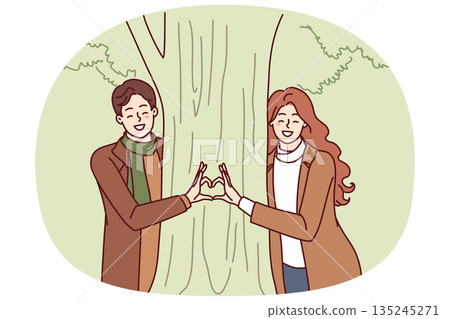 Couple stands near tree together making heart from their fingers as sign of love for partner 135245271