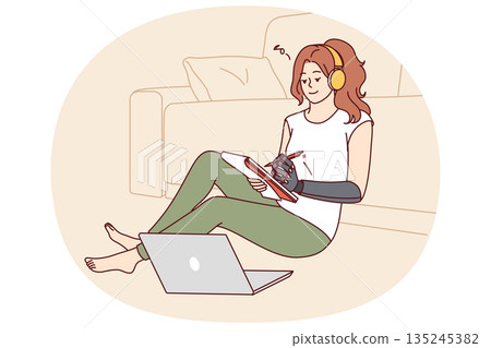 Woman with bionic prosthetic arm sits on floor near sofa and makes notes in notebook 135245382