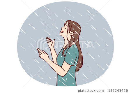 Woman enjoys rain standing under drops falling from sky in wet t-shirt and raising head up Woman enjoys rain standing under drops falling from sky in wet t-shirt and raising head up 135245426