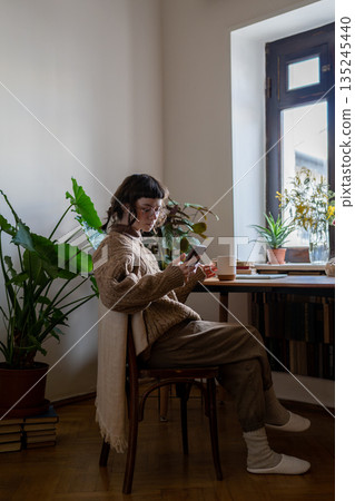 Thoughtful girl student sits at desk with cup, reading news in cellphone procrastination of homework 135245440