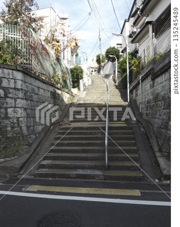 A long staircase in a residential area leading up to the blue sky. A deep slope surrounded by stone walls and a calm everyday winter scene. 135245489
