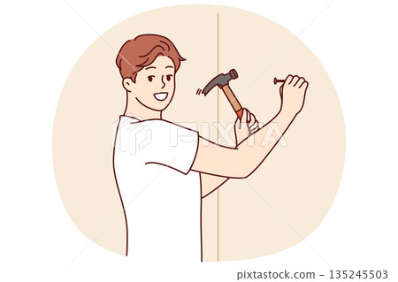 Man with hammer makes repairs in house by hammering nail into wall to hang picture Man with hammer makes repairs in house by hammering nail into wall to hang picture 135245503